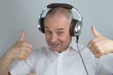 Olgun karizmatik bir adamın 60 yıl kulaklık takıp yüz hareketleriyle müzik dinlemesi, açık gri arka planda konsept öğrenmesi, yabancı dil öğrenmesi, canlı yayın ve vloglama