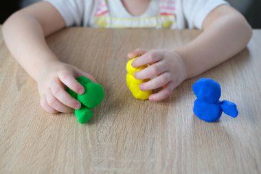Küçük bir çocuğun, sarışın bir kızın ellerinde plastik oyuncaklar. 2 yaşında heykeller, renkli hamurdan karakterlerin figürleri. Güzel motor beceriler kavramı, dokunsal hisler, yaratıcılık.