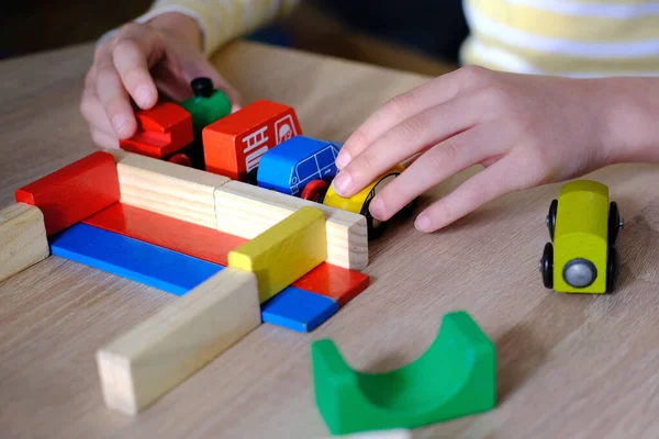 close-up of child\'s hands holding colored wooden cubes, dominoes, child 7-9 years old builds houses, rolls cars, concept of construction game, development of creativity, fine motor skills, patience