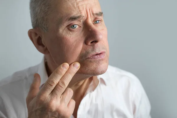 特写有魅力的成熟男子60岁时在脸上涂上剃须后护理 批判性地检查面部 因年龄变化而烦躁不安 中年危机 选择性焦虑症 — 图库照片