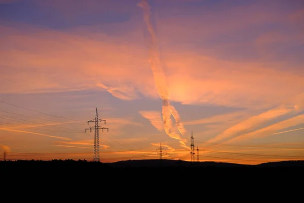 beautiful dramatic landscape, sky with airplane trail lines, power towers, field in evening in rays of sunset, concept of beauty of nature, modern energy, technology, black hills at bottom