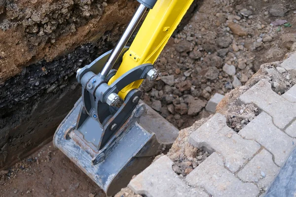 excavator bucket digs earth in trench on street, concept of repairing urban communications, conducting electrical networks to buildings, underground laying optical fiber for communication