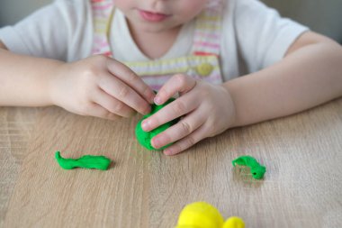 Küçük bir çocuğun, sarışın bir kızın ellerinde plastik oyuncaklar. 2 yaşında heykeller, renkli hamurdan karakterlerin figürleri. Güzel motor beceriler kavramı, dokunsal hisler, yaratıcılık.