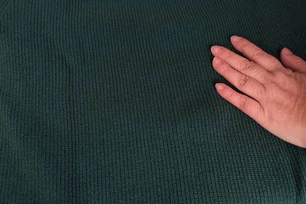 close-up of female hand touches knitted jersey, embossed canvas, green wool yarn, knitted texture, concept of warm things for cold weather, check quality, fashionable clothes, clothing production