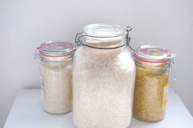 Kapaklı cam kavanozlarda çiğ beyaz ve esmer pirinç yağmurlu günler için stratejik gıda stokları, yemek malzemeleri, ekolojik ambalaj, haşere kontrolü.