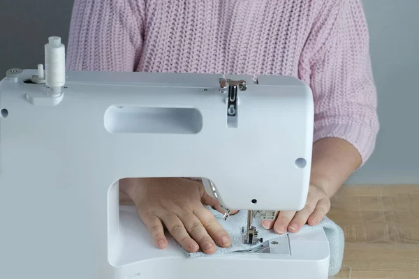 close-up of female hands perform work on white sewing electric computer machine, stitches appear step by step on fabric, concept of tailoring, women\'s hobby, seamstress profession, modern needlework