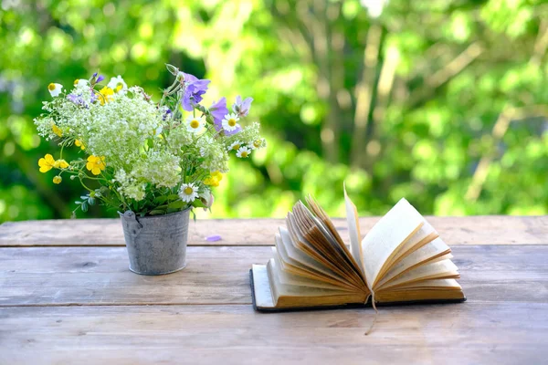 Siyah kaplı açık bir kitap, aile incili, bir buket yabani çiçek bahçedeki ahşap masa, arka planda bulanık doğal manzara yeşil yapraklar, kavram eğitimi, bilgi, Hıristiyan dini