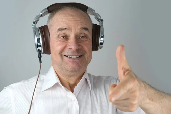 close-up of mature charismatic man 60 years in headphones listening to music with emotions on face gestures, on light gray background, concept learning foreign languages, live streaming and vlogging
