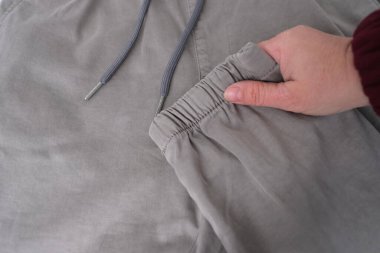 Kadın elinin yakın çekimi gri pamuk pantolon desenine dokunur. Cebinde deri pantolon, bileğinde kelepçe, belinde ip, içine bakar. Şah kalitesi kavramı, modaya uygun kıyafetler.