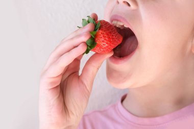 Çocuğun elinde taze çilek, 14-15 yaşlarında neşeli bir kız, taze vitamin meyvesi, ağızda lezzetli böğürtlen, sağlıklı beslenme konsepti, çocuklar için sağlıklı yemek, iyi bir iştah.