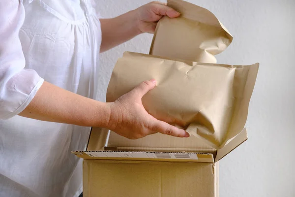 close-up of female hands take out package from open cardboard box of medium size postal box with wrapping paper, a parcel, delivery of ordered goods, online shopping, timely delivery to customers