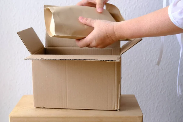close-up of female hands take out package from open cardboard box of medium size postal box with wrapping paper, parcel, delivery of ordered goods, online shopping, timely delivery to customers