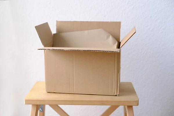 an open cardboard box of medium size stands on a wooden stool, a postal box with wrapping paper, a parcel, delivery of ordered goods, online shopping concept. Mockup for design