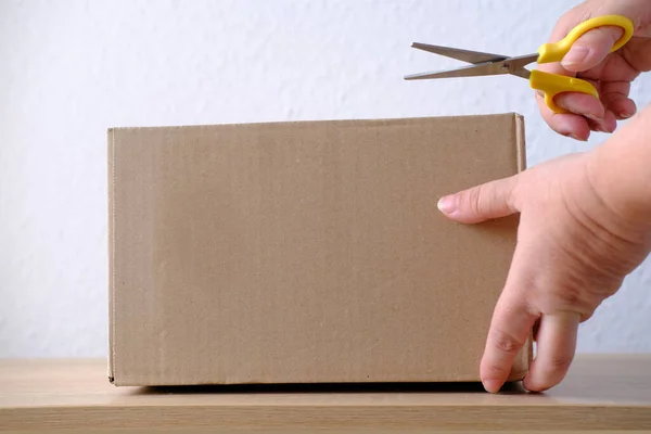 close-up of female hands open cardboard box of medium size stands on wooden stool, postal box with wrapping paper, a parcel, delivery of ordered goods, online shopping, timely delivery to customers