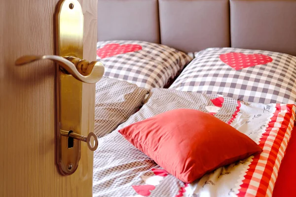Open door with key in the keyhole in the hotel room on the bed, heart-shaped blanket, two pillows, red cotton bed linen, the concept of healthy sleep, insomnia problems, a cozy stay in a hotel