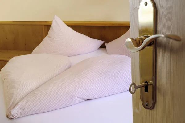 Open door with key in the keyhole in the hotel room on the bed, heart-shaped blanket, two pillows, white cotton bed linen, the concept of healthy sleep, insomnia problems, a cozy stay in a hotel