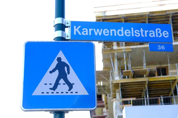 blue pedestrian crossing sign, street name karvendelstrasse in german, part of the construction site in the background, pedestrian zone concept, traffic safety for people