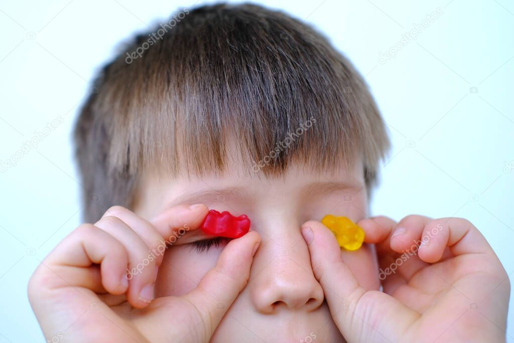 close-up of part of child, boy 7 years old holds candy to the eyes and eats gelatinous sweets, gummy bear, concept of children's delicacy, healthy and unhealthy food, halal food