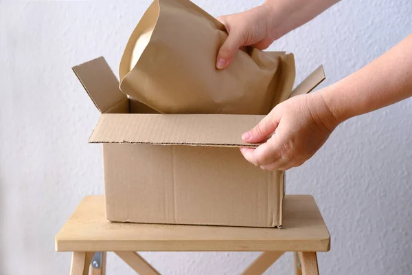 close-up of female hands take out package from open cardboard box of medium size postal box with wrapping paper, a parcel, delivery of ordered goods, online shopping, timely delivery to customers