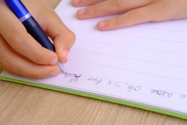 child, schoolboy 9-10 years, primary school student writes in notebook, Back to school concept, children's hand close-up, doing homework in foreign language, spelling skills, intense school load