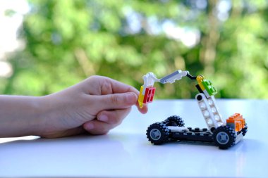 Çocuğun parmakları transformatör arabayı manipülatörle hareket ettirir, lego parçalarından, yeşil arkaplandan, konsept geliştirmeden, iyi motor beceriler, yaratıcılık, çocuk eğlencesi, Frankfurt - Haziran 2022