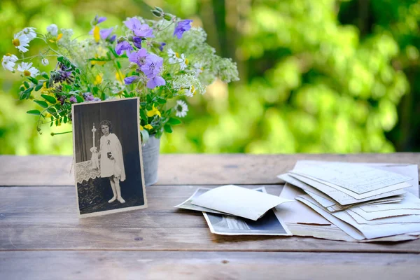 old vintage photographs, bouquet of wild flowers on table wooden table in garden, beautiful blurred natural background with green foliage, concept of genealogy, memory of ancestors, family tree