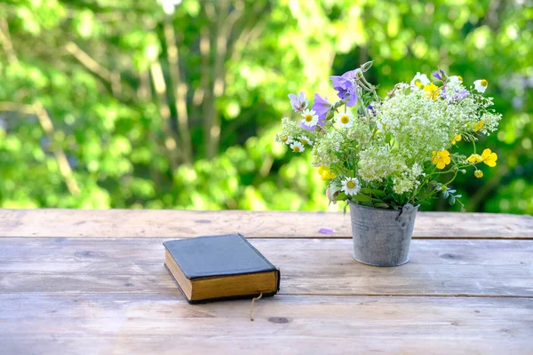 黒い表紙の本野生の花の花束聖書は庭の木のテーブルの上にあり緑の葉を背景に自然の風景をぼやけている概念教育知識キリスト教宗教 — ストック写真