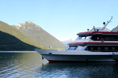 Sudaki turistik tekne romantik göl konsepti, deniz yolculuğu, yat, tekne, turistik tekne, sakin suların üzerinde yükselen yeşil dağlar.