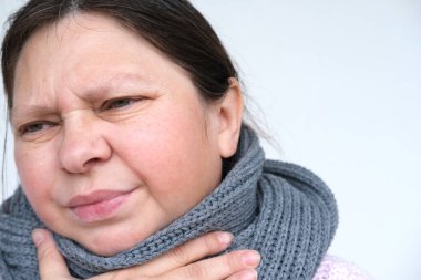 Olgun bir kadının 55 yıllık yüzü, atkıya sarılmış boynu, iltihaplı gözleri, acıdan muzdarip hasta bir insan, hastalık, ateş, kötü ruh hali, hoşnutsuzluk, boğaz ağrısı.