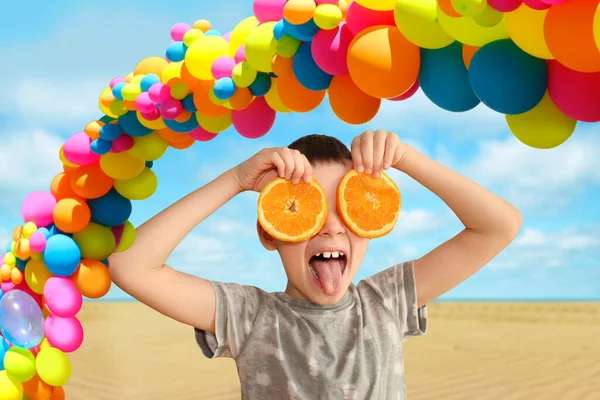 two orange slices of fresh, juicy oranges holding a cheerful kid in their hands on a bright background, holiday balloons bright colors, concept of vitamins, birthday party, holiday, family celebration