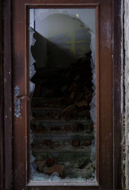 dirty broken door frame with hole in center, sharp pieces of glass sticking out, concept shot, military operations, destruction of buildings from bombing and rocket attacks, blast wave