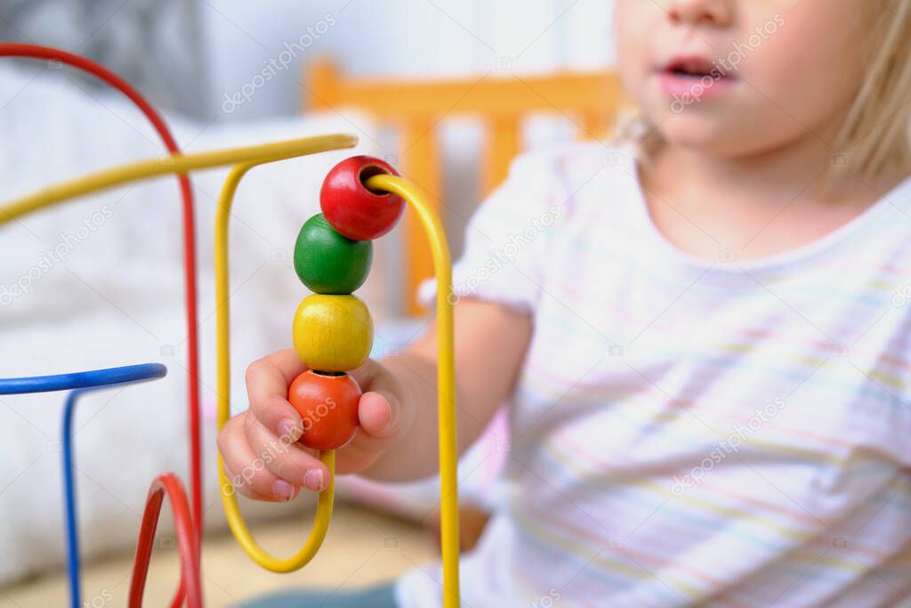 girl 3 years old plays with colored wooden educational labyrinth for kids, close-up of hands of cute child, development of fine motor skills, concept of development of creativity, interest in toys