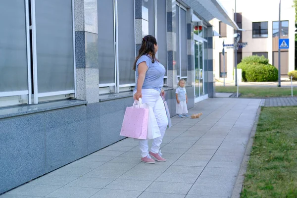 happy mom and daughter hold shopping bags together, woman and child of 3-4 years old go out of store, girl is behind, the mother is waiting, shopping concept, happy shopping on Black Friday