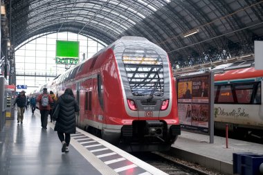EuroCity red train of Deutsche Bahn on platform of Frankfurt am Main station, passengers with luggage and backpack go to board train, concept of boarding travelers in cars, Frankfurt - January 2022