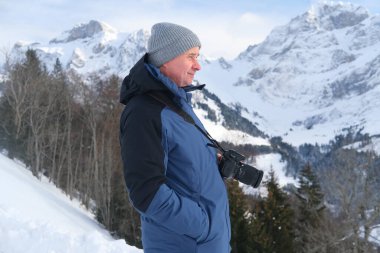 Kameralı yaşlı bir adam, dağ yürüyüşçüsü kış manzarasına hayran, spor konsepti, sağlıklı yaşam tarzı, kış etkinliği, güzel kış doğal manzarası, kışın beyaz ormanda yürüyor.