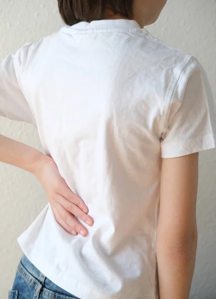 part of naked back of boy, child 10 years old in a white t-shirt, grabbed a sore spot, concept of therapeutic massage for osteochondrosis, scoliosis, back pain, intervertebral hernia