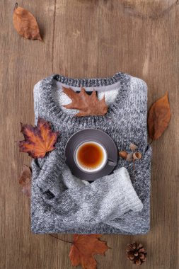 wooden table, tea, coffee in a mug stands on a gray men's jumper with dry brown leaves around, the concept of good weather, a cozy autumn mood