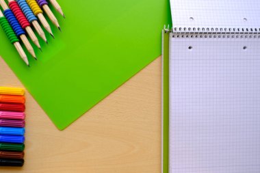 school background, colored pencils lie on a sheet of paper, open notebook on a spiral, college block in a cage, close-up, concept student writing materials, back to school