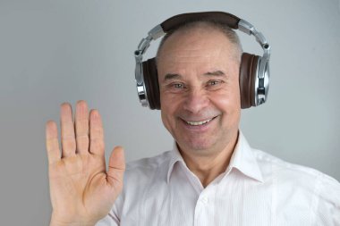 Olgun karizmatik bir adamın 60 yıl kulaklık takıp yüz hareketleriyle müzik dinlemesi, açık gri arka planda konsept öğrenmesi, yabancı dil öğrenmesi, canlı yayın ve vloglama