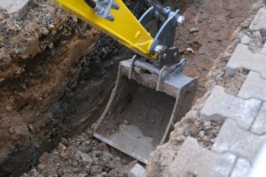 Kazı kovası toprağı sokak siperlerinde kazıyor, kentsel iletişimi onarma konsepti, binalara elektrik şebekeleri kurma, yer altında iletişim için optik fiber döşeme