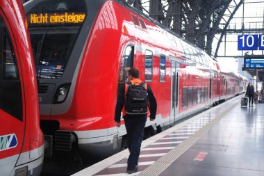 modern red train of Deutsche Bahn on platform of Frankfurt am Main station, passengers with luggage and backpack go to board train, concept of boarding travelers in cars, Frankfurt - January 2022