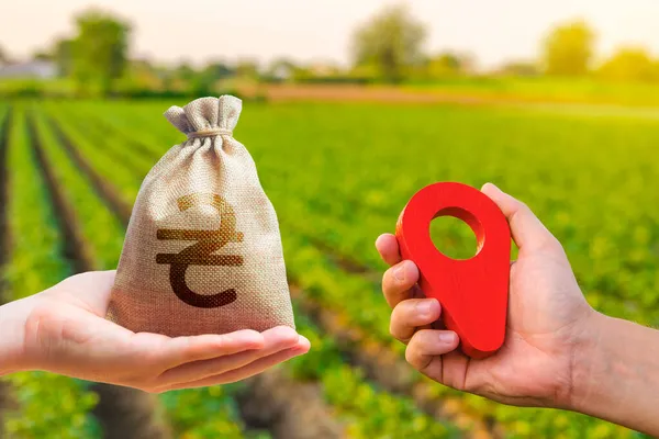 Hands with location pin and ukrainian hryvnia money bag. Land market. Estimation cost of plots. Agriculture agribusiness. Transport and construction industry. Buying and selling land.