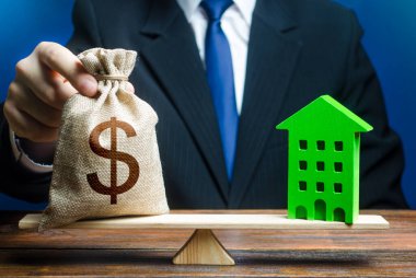 İşadamı teraziye ve yeşil eve dolar çantası koyuyor. Çevre teknolojilerinin karlı konutları. Tadilata yatırım. Karbondioksit salınımını azaltmak, enerji verimliliği. Geri ödeme süresi