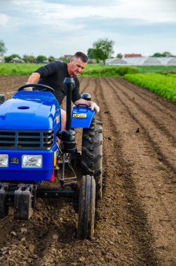 Kherson oblast, Ukraine - May 29, 2021: Senior farmer is working on a tractor. Seasonal worker. Recruiting workers with skills in driving agricultural machinery. Milling soil before cutting rows. clipart