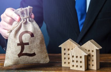 British pound sterling money bags and residential buildings figures. Taxes. Bank offer of mortgage loan. Rental business. Sale of housing. Buy. Investments in real estate and construction industry.