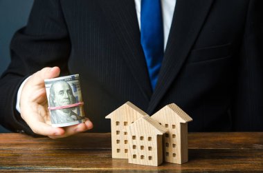 Gayrimenkul piyasası. İşadamı ahşap evlerin yanında dolarları tutuyor. Yatırımlar ve ipotek. Bütçe, krediler. Bir ev alıp kiralamak. Uygun fiyatlı konut