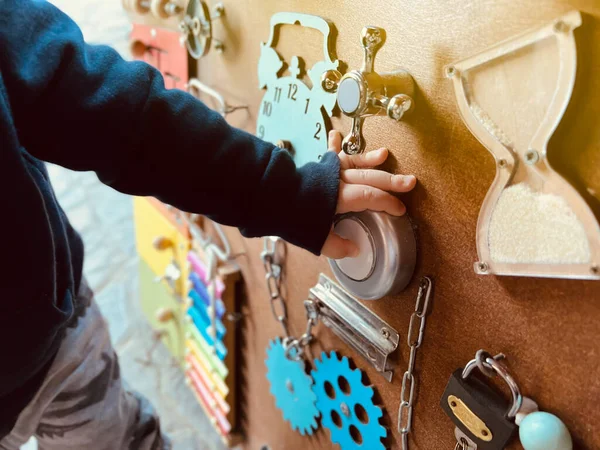 A little boy is playing with a busy board. Developming toy for children from one year old. Developming toy for children from one year old. Selective focus