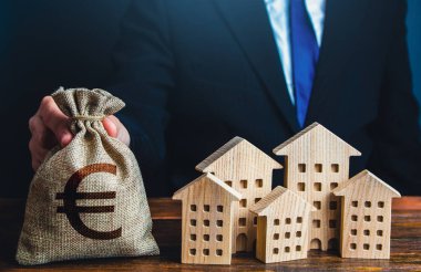 A businessman puts a euro money bag near the houses. Investments in real estate assets. Municipal budget of the city. Official. Construction industry, rental business and hotel tourism.