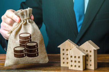 Money bag in a hand and residential buildings figures. Investments in real estate and construction industry. Bank offer of mortgage loan. Rental business. Sale of housing. Buy. Municipal budget. Taxes