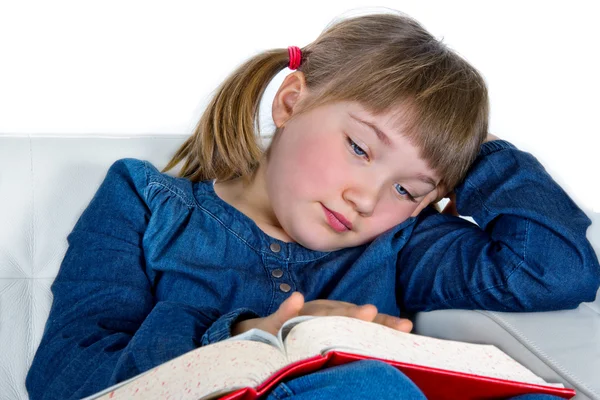 Menina bonito ler um livro sentado em um sofá — Fotografia de Stock